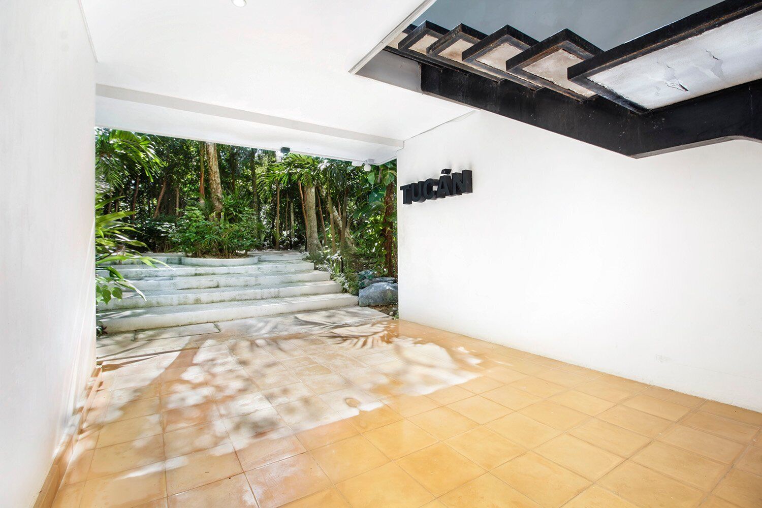 Una escalera conduce a un jardín con un muro blanco y un cartel negro.