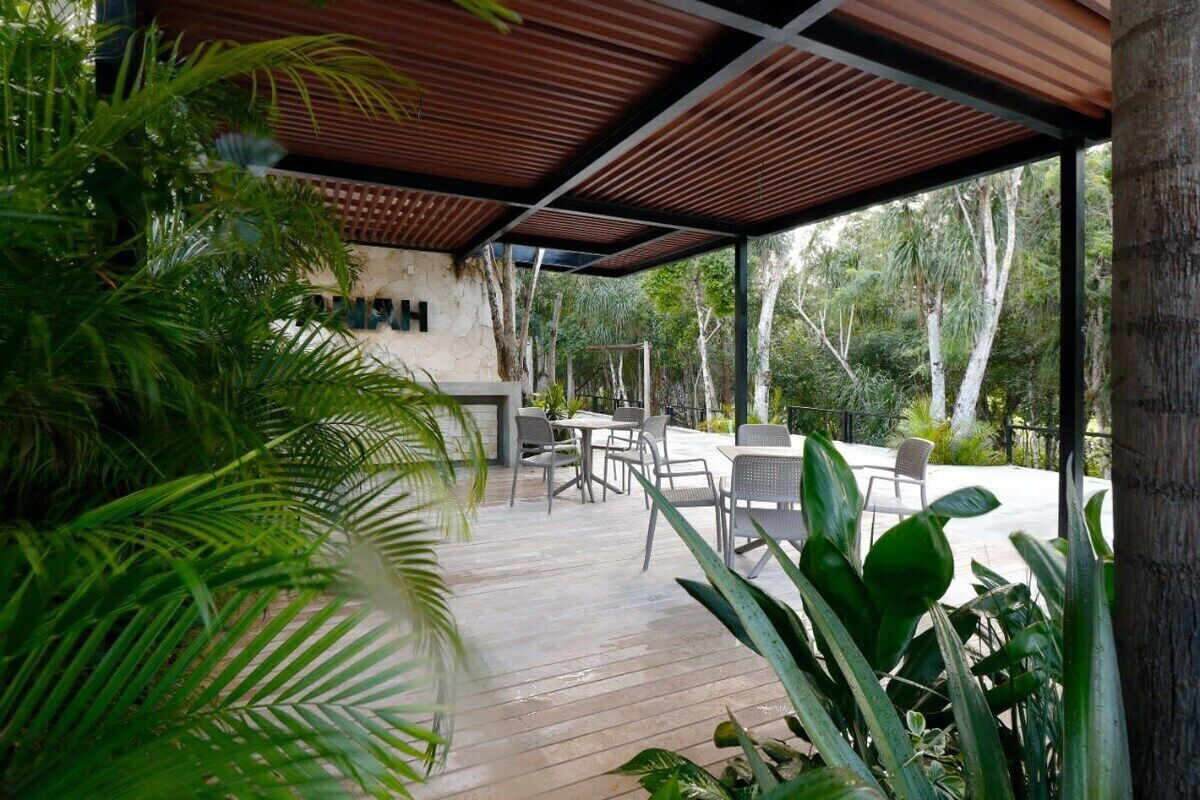 Area patio esterna con pavimento in legno, tavoli e sedie dalla struttura in metallo e rigogliosa vegetazione.