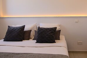 A neatly made bed with a white bedspread and multiple pillows, including a black quilted one. - Phaedrus Living: Seaside Executive Flat Harbour 207 (Paphos)
