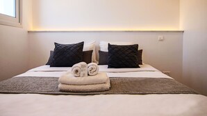 A neatly made bed with a folded towel and a note, two black pillows, and a grey throw blanket. - Phaedrus Living: Seaside Executive Flat Harbour 207 (Paphos)