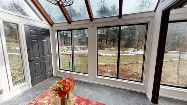 A room with large windows, a door, and a vase with flowers on a table. - Winter Lore (Rutland)