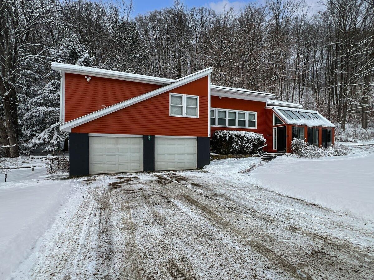 Une maison rouge avec deux portes de garage, un porche couvert et une allée enneigée.