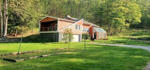 A two-story house with a large porch, surrounded by a well-maintained lawn and trees. - Winter Lore (Rutland)