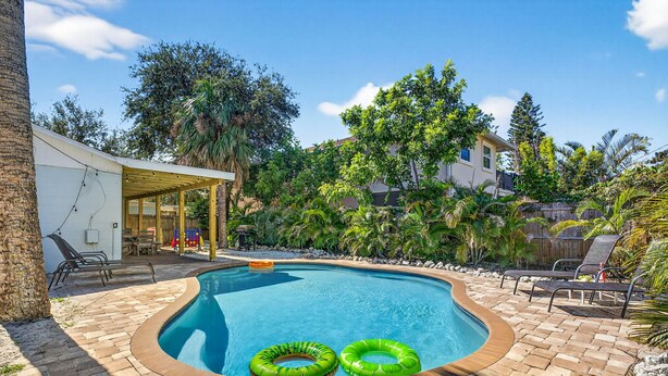 A swimming pool with two green inflatable rings, surrounded by a brick patio and shaded by trees. - Heated Pool/2 min walk 2 the Beach/Sleeps 9/Cute (Indian Rocks Beach)