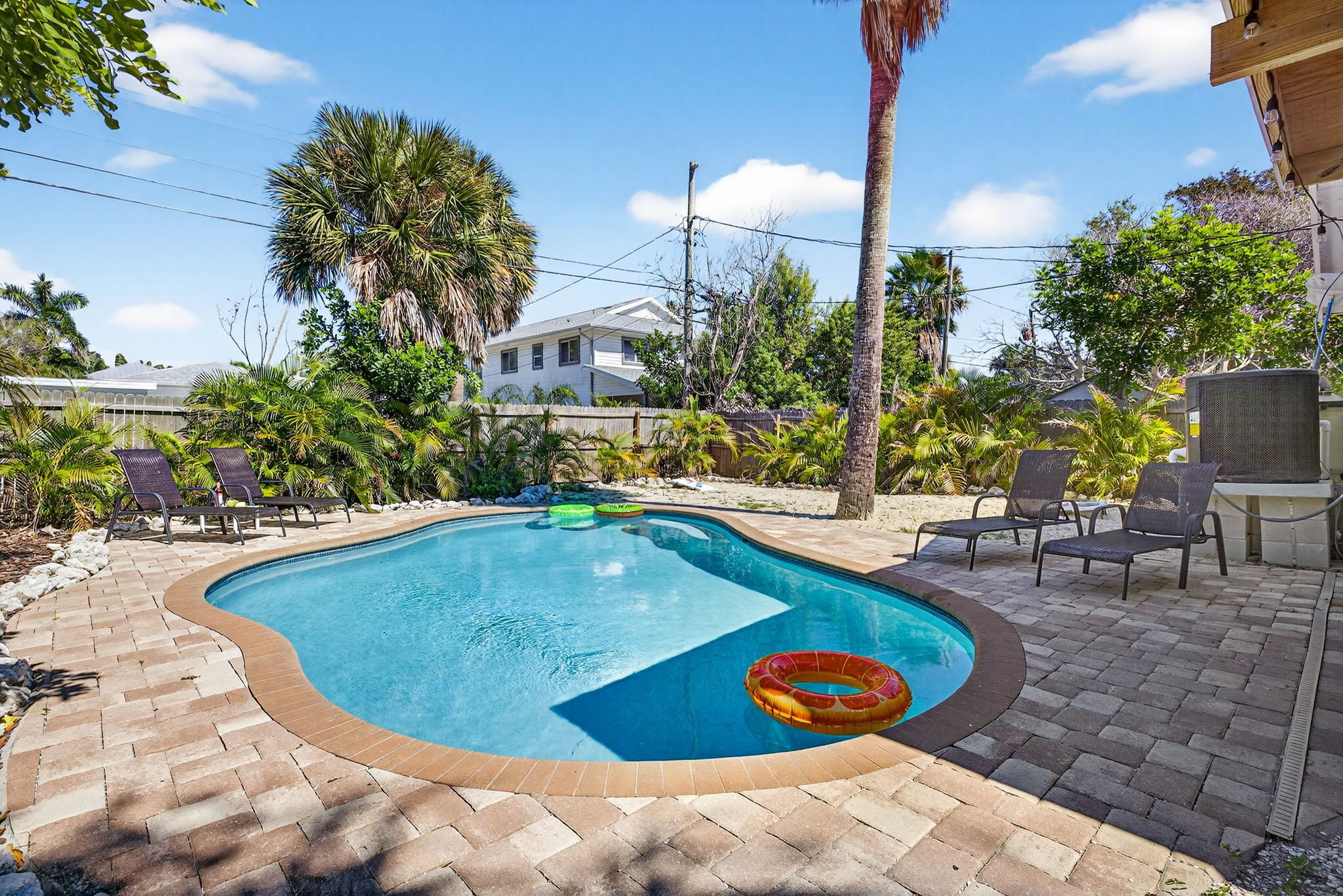 A swimming pool with a curved edge, surrounded by a brick patio and palm trees.