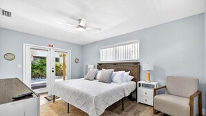 A bedroom with a bed, nightstands, a chair, a ceiling fan, and a view of the outdoors. - Heated Pool/2 min walk 2 the Beach/Sleeps 9/Cute (Indian Rocks Beach)