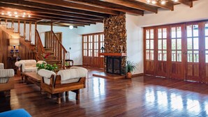 Un salon spacieux doté d’un plancher en bois, d’une cheminée en pierre, d’un escalier en bois et de grandes fenêtres.