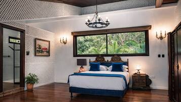 Quarto com uma grande janela, cama com roupa de cama azul, um candelabro e um vaso de planta.