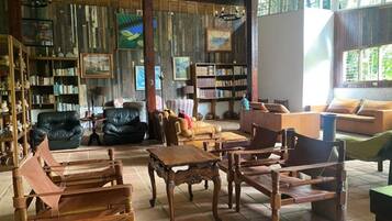 A spacious room with a large wooden table, multiple seating options including a sofa and chairs, a bookshelf filled with books, and a large window providing natural light.