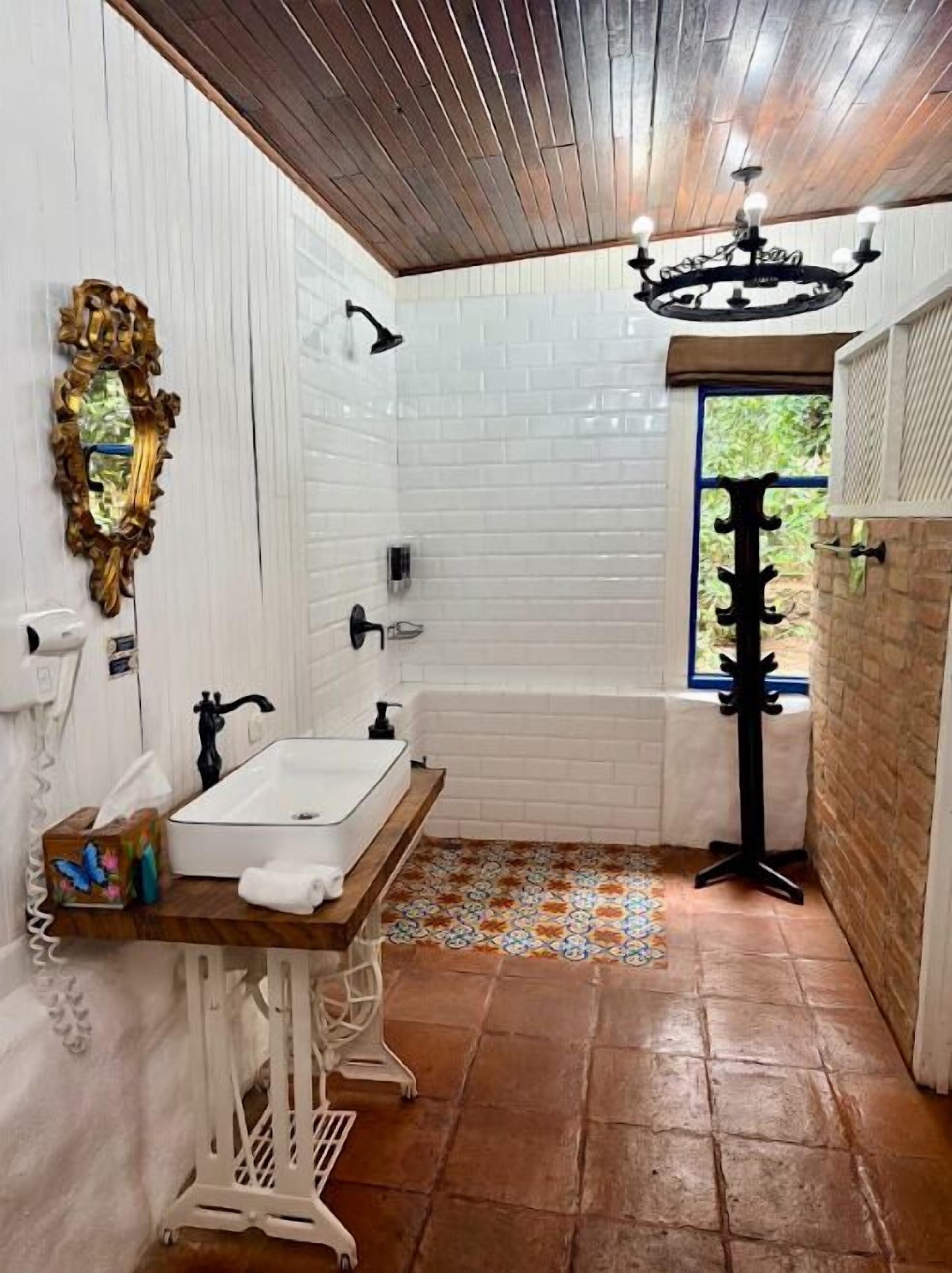 A bathroom with a white sink, wooden vanity, and a black chandelier.