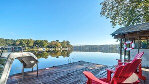 A wooden dock with red Adirondack chairs and a lifebuoy, overlooking a calm lake with a clear sky. - **Family Retreat w/ Lake FRONT View (4bdr) (DeKalb County)