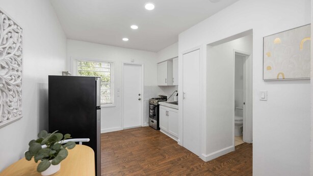 Una cocina moderna con armarios blancos, un refrigerador negro y una mesa de comedor de madera con una planta.