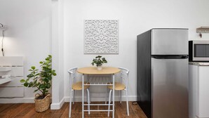 Una cocina compacta con un refrigerador blanco, un microondas, una pequeña mesa con dos sillas y un adorno en la pared.