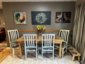 Un coin repas avec une table en bois, quatre chaises et un vase rempli de tournesols. Trois œuvres d’art sont accrochées au mur au-dessus de la table.