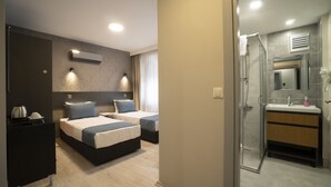 Habitación de hotel con dos camas, una kitchenette pequeña y un baño con cabina de ducha de vidrio.