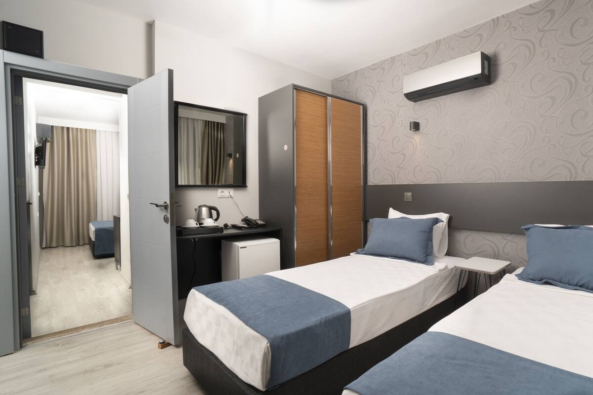 A modern hotel room with two beds, a desk, a wardrobe, and an air conditioning unit.