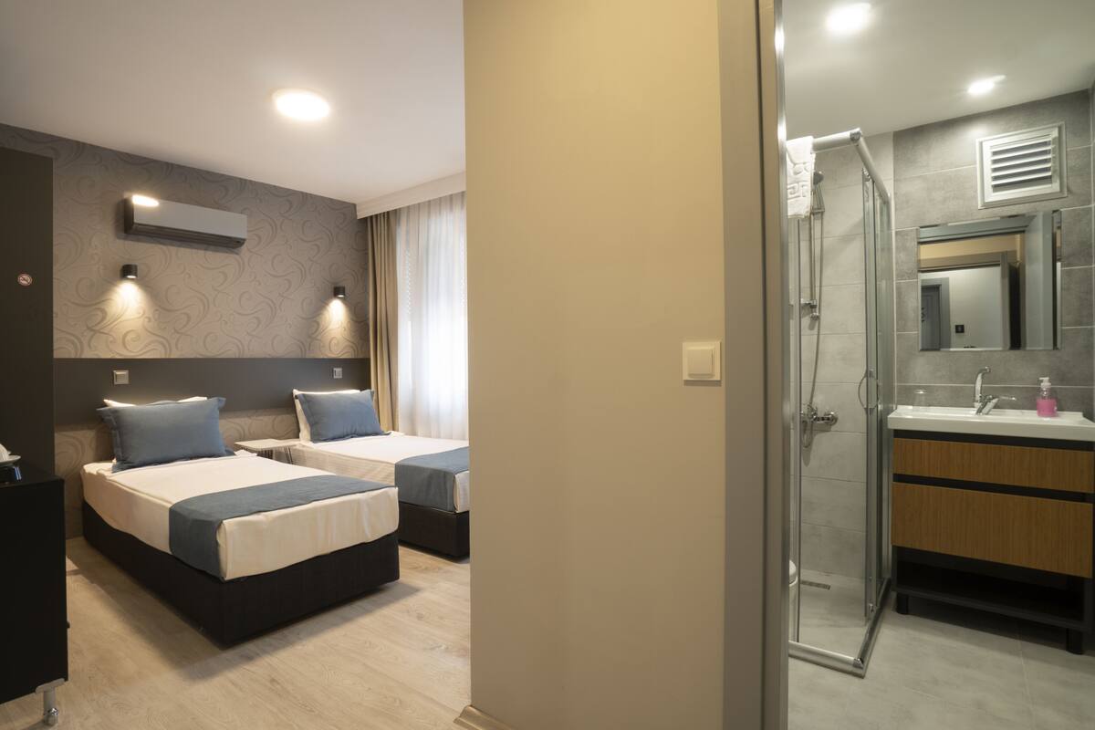 A hotel room with two beds, a bathroom with a shower, and a coffee maker on the desk.