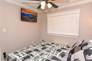 Une chambre à coucher avec un lit, un ventilateur de plafond, une fenêtre avec des volets et un tableau au mur.
