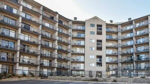 Un immeuble résidentiel à plusieurs étages, doté de balcons, d’une entrée principale et d’un parking situé à l’avant.