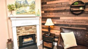 Un salon avec une cheminée, un tableau accroché au mur, un lambris en bois, un canapé en cuir et une table d’appoint avec une lampe.