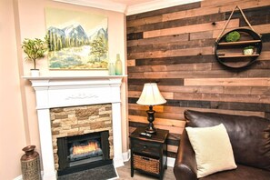 Un salon avec une cheminée, un tableau accroché au mur, un lambris en bois, un canapé en cuir et une table d’appoint avec une lampe.
