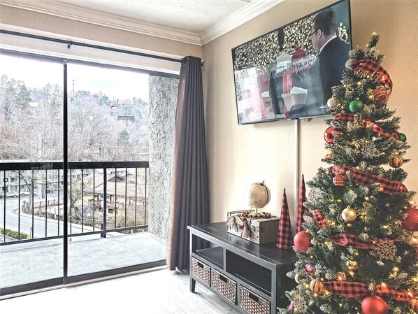 A living room with a large window, a Christmas tree, a flat-screen TV, and a console table with a globe and a candle.
