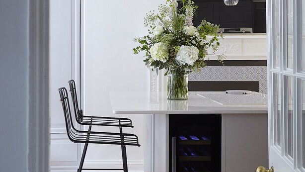 Una cucina moderna con un piano di lavoro bianco, una sedia nera e un vaso di fiori.