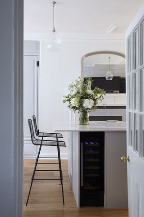 Une cuisine moderne avec un plan de travail blanc, une chaise noire et un vase de fleurs.