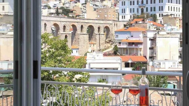 A balcony with a table and chairs, overlooking a historic stone bridge and a densely packed cityscape.