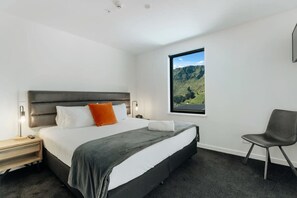 A modern hotel room with a large bed, a nightstand, a chair, and a window with a mountain view. - La Residence du Parc - 7 (Queenstown)