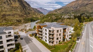 Ett modernt bostadskomplex med flera balkonger, en flod i bakgrunden och ett bergigt landskap.