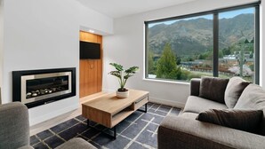 A modern living room with a fireplace, a large window with a mountain view, and a cozy seating area. - Coronet Bliss at La Residence du Parc (Queenstown)