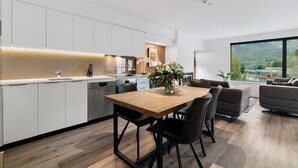 A modern kitchen with white cabinets, a wooden dining table, and a view of the outdoors. - Coronet Bliss at La Residence du Parc (Queenstown)