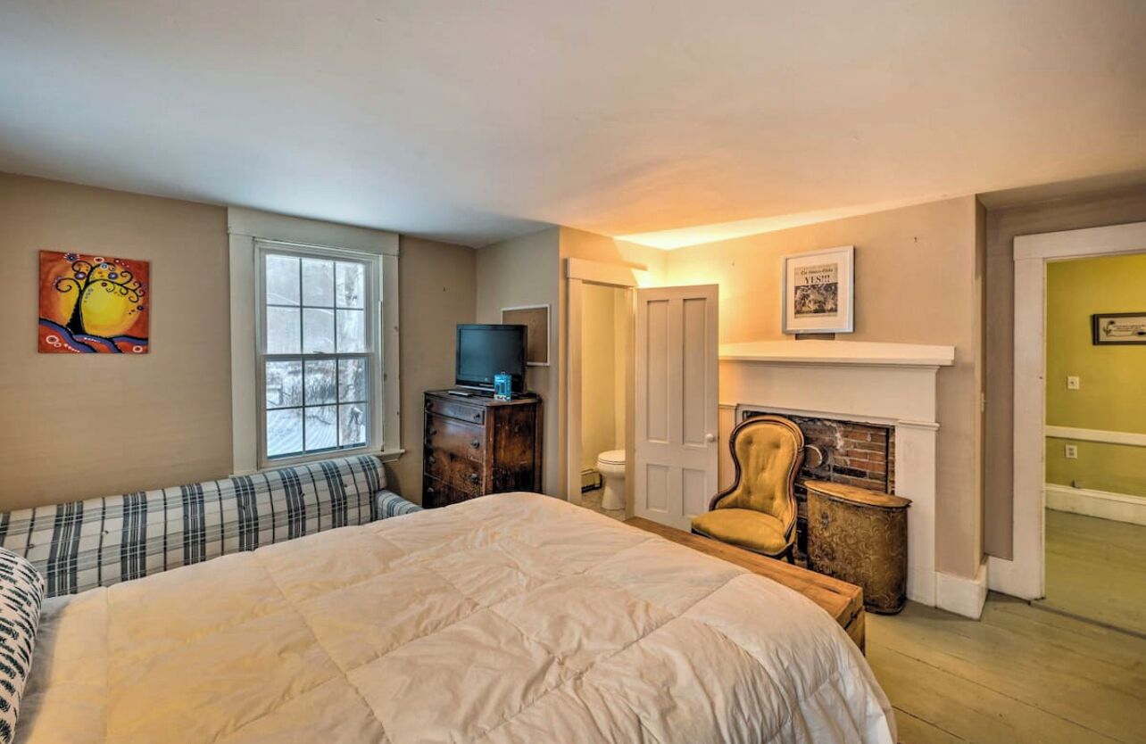A bedroom with a large bed, a dresser, a television, a chair, and a fireplace.