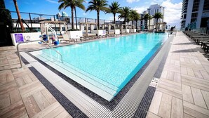 A swimming pool with a tiled deck, palm trees, and a cityscape in the background.