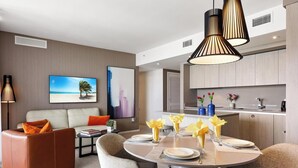 A modern living room with a sofa, dining table set with yellow napkins, and a kitchen area with a sink and cabinets.