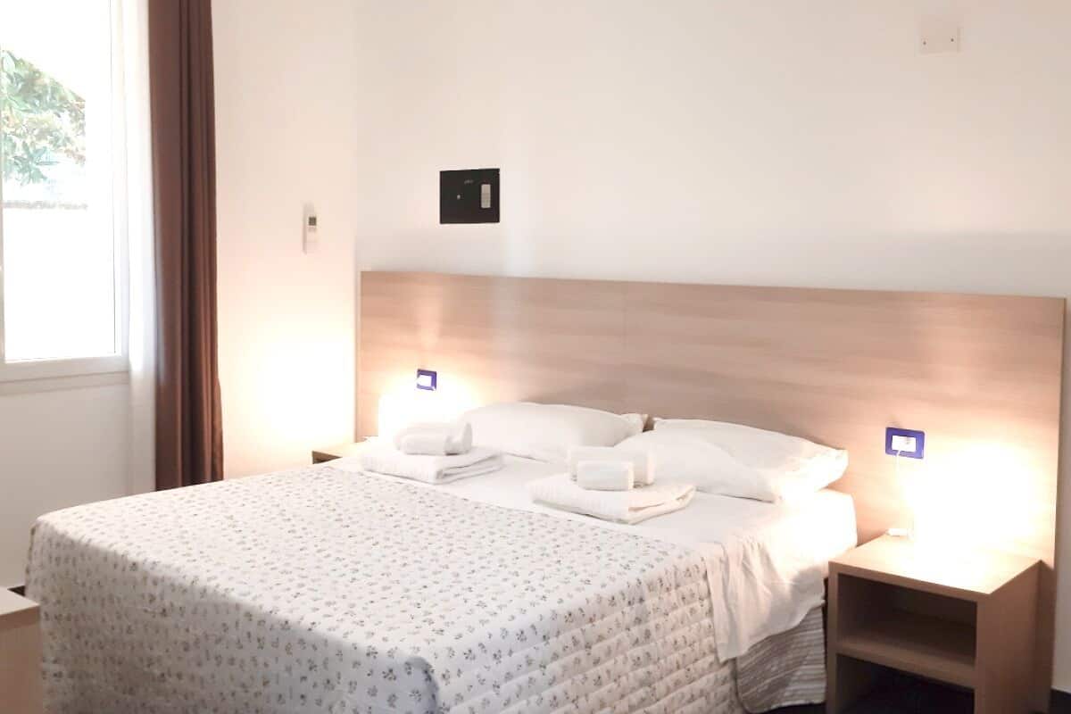 A neatly made double bed with a headboard, two bedside tables, and a window with curtains.