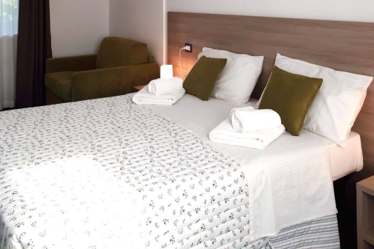 A hotel room with a bed, a bedside table, a lamp, and a chair.