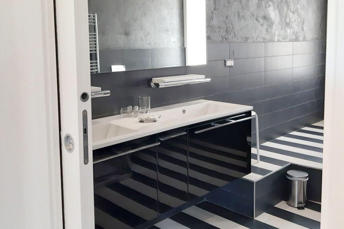 A modern bathroom with a large mirror, a white sink, and a striped floor.