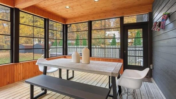 A wooden deck with a table and chairs, large windows, and a door.
