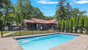 A swimming pool with a house in the background, surrounded by a fence and trees.