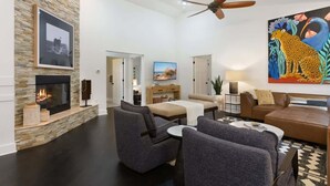 A spacious living room with a fireplace, modern furniture, a ceiling fan, and artwork on the walls.