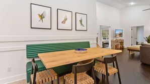 A dining area with a wooden table, green cushioned bench, and framed bird paintings on the wall.