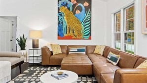 A living room with a brown leather sofa, a white coffee table, and a colorful abstract painting on the wall.