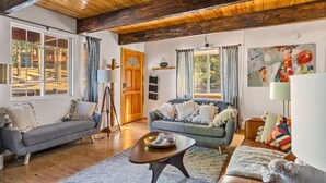 A cozy living room with wooden beams, two sofas, a coffee table, and a door leading outside.
