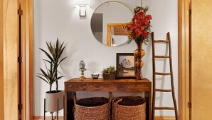 A wooden dining table with a mirror, a vase with flowers, a framed picture, and a ladder leaning against the wall.