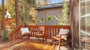 A wooden deck with chairs and a small building in a forested area.