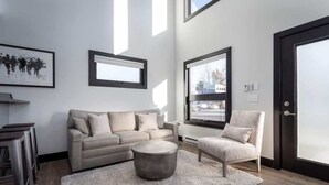 Ein modernes Wohnzimmer mit einer Couch, einem Sessel, einem runden Couchtisch und einem großen Fenster.