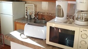 A kitchen with wooden cabinets, a white refrigerator, a microwave, a coffee maker, and a sink. - Recreational Vehicle (Vilamoura)