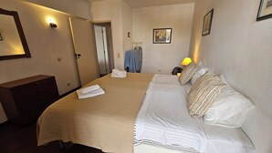 A hotel room with a bed, a bedside table, a wardrobe, a mirror, a wall-mounted light, and a picture. - Recreational Vehicle (Vilamoura)